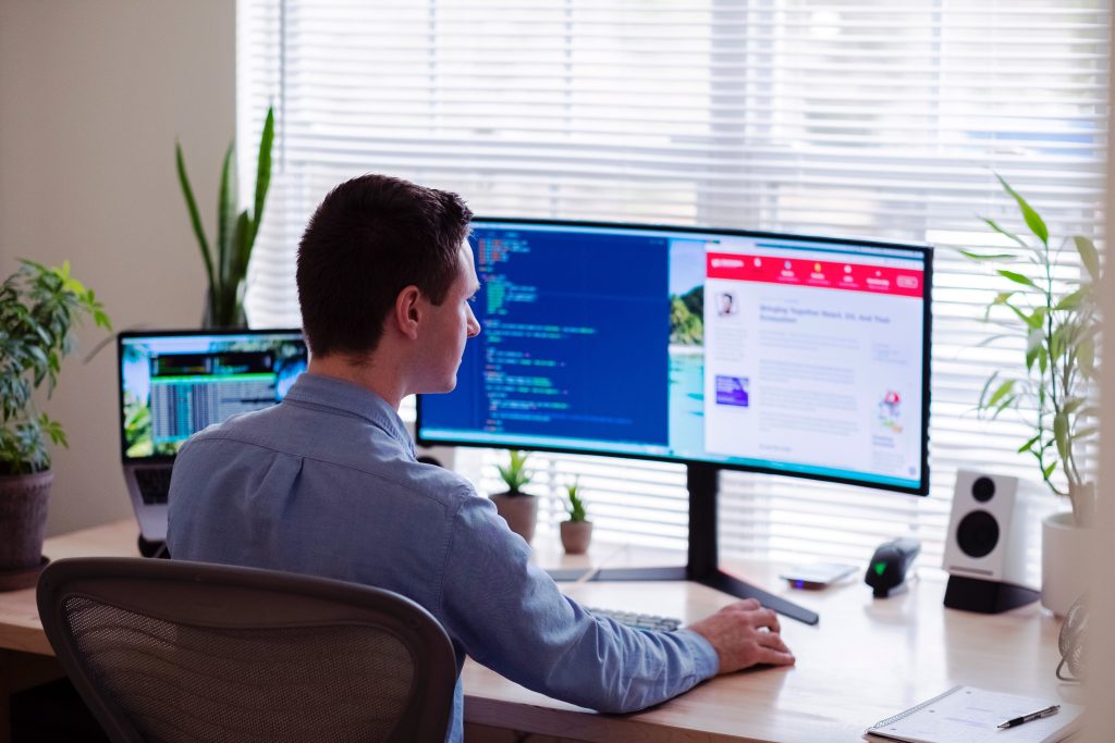 Remote Working Professional working remotely at a desk with multiple monitors, laptop, and code on screen.