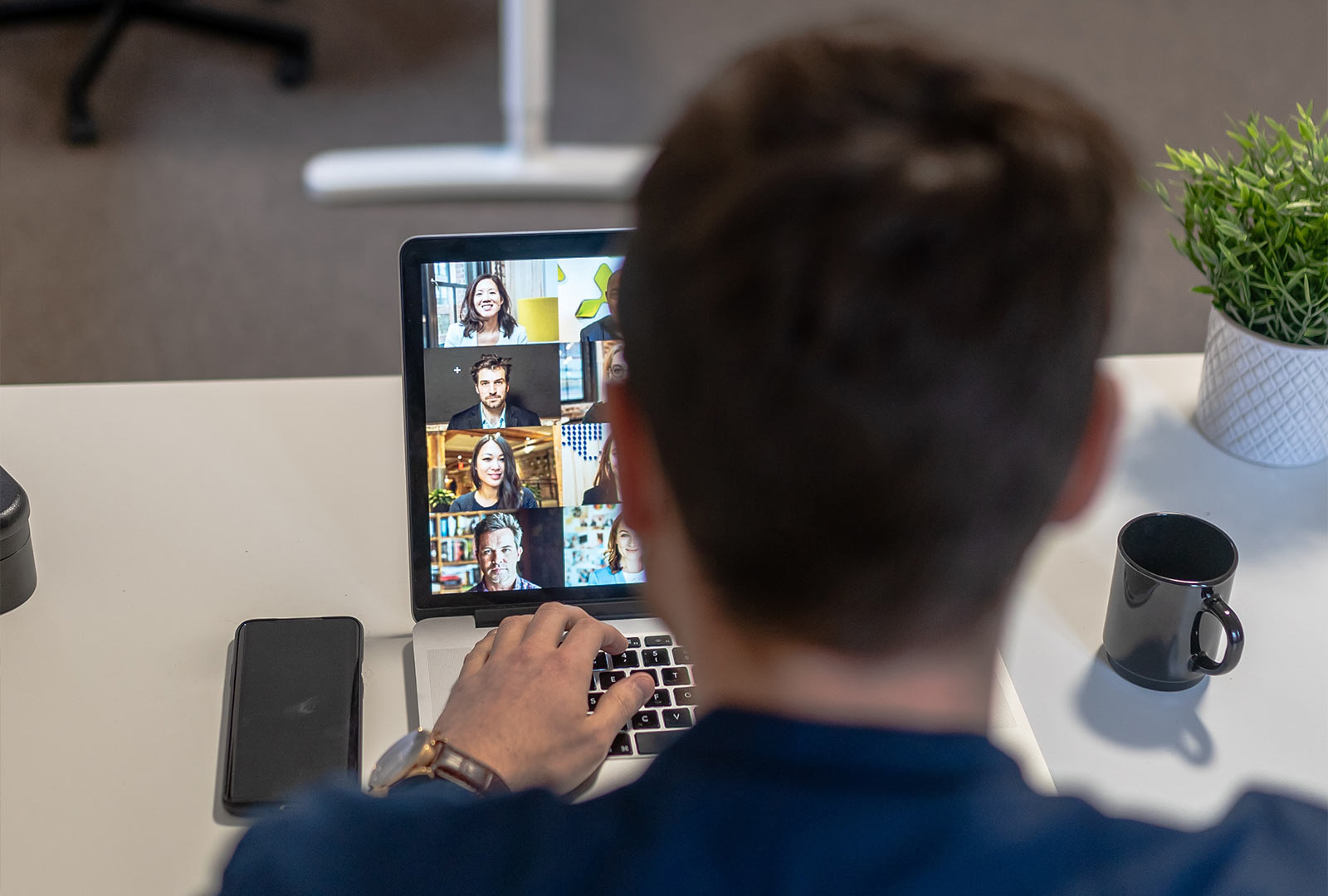 Professional joining a video call on a laptop with remote team members shown on screen.