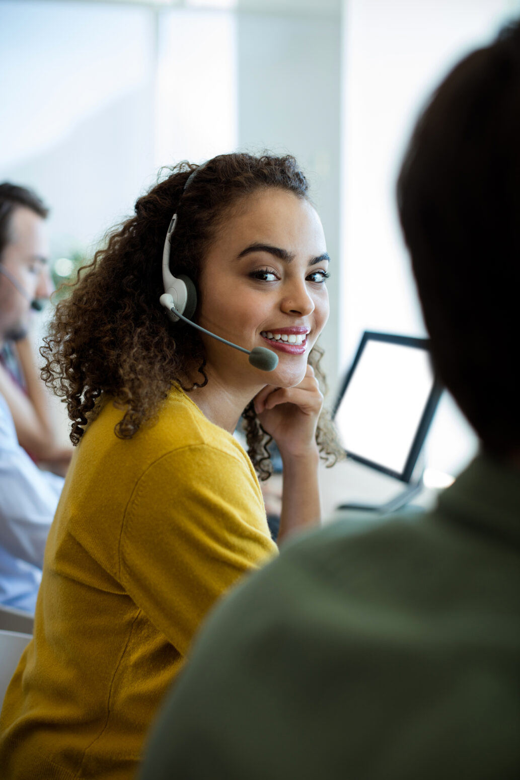 Customer support representative wearing a headset while speaking with a person in a modern office.