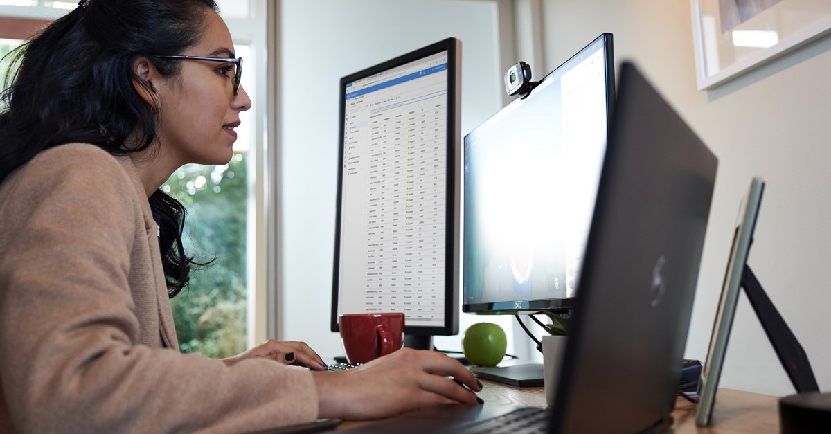 Professional using dual monitors and a laptop, representing Microsoft moving to NCE licensing.