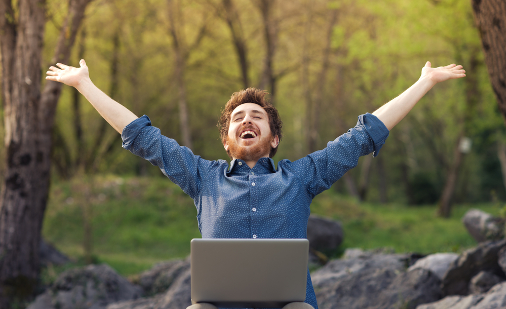 Man using a laptop outdoors with arms raised, representing Office 365 apps making work easier.