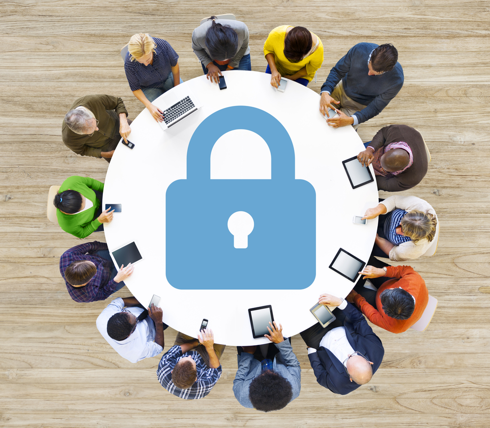 Group using devices around a table with a large lock icon, representing social media security.