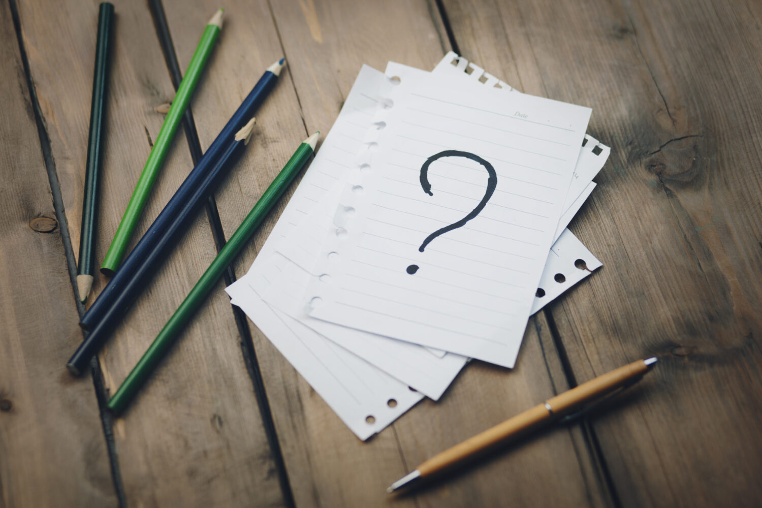 Notebook paper with a question mark and pencils, representing questions for hiring an IT management company.