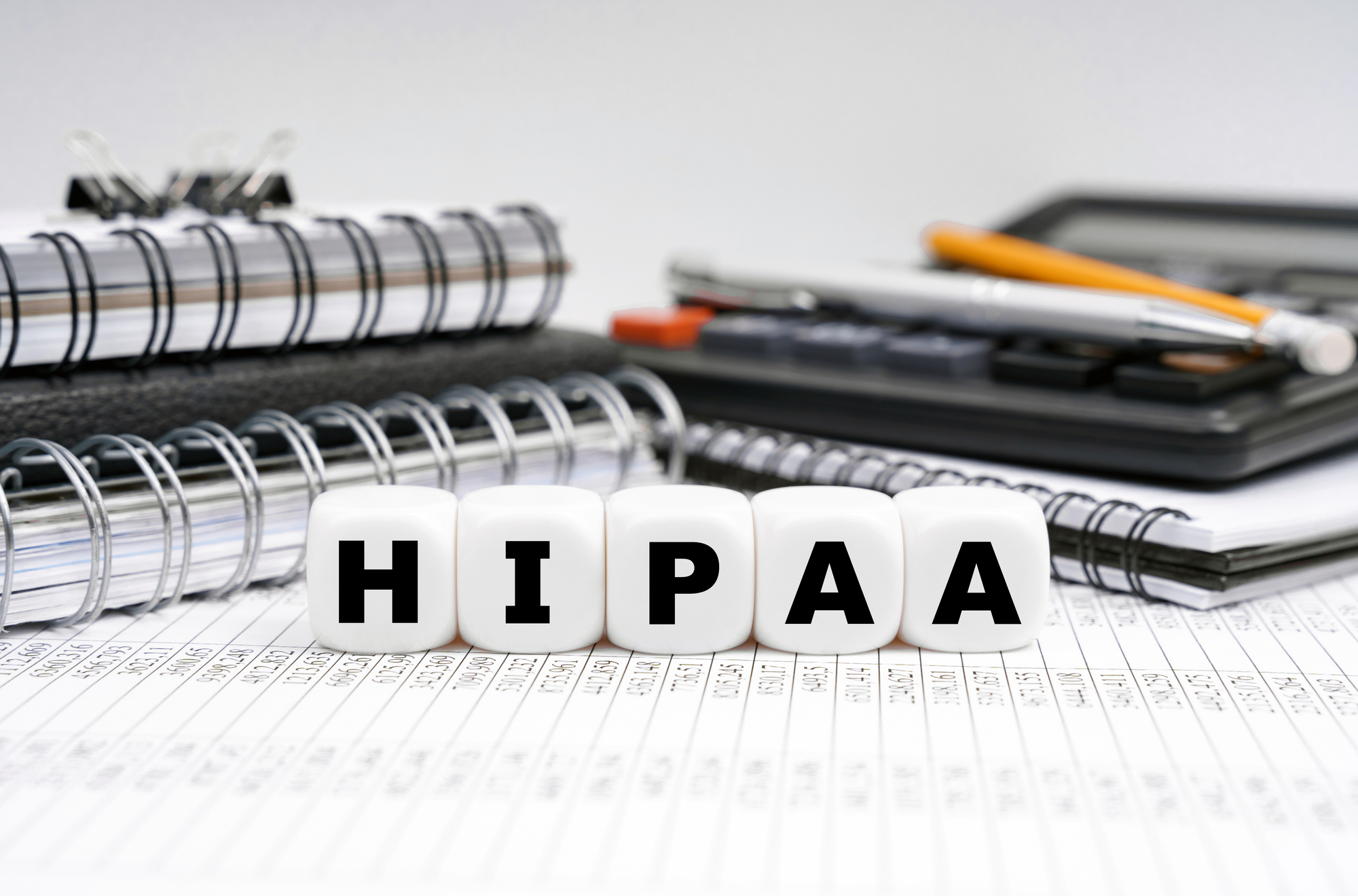 HIPAA letter blocks on paperwork with notebooks and calculator, representing healthcare compliance.