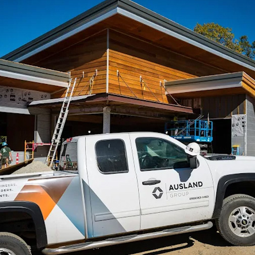 Construction site with an Ausland Group branded truck parked outside, and workers on a ladder and scaffold near the building. Construction site with an Ausland Group branded truck parked outside, and workers on a ladder and scaffold near the building.