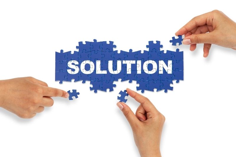 Hands assembling a blue jigsaw puzzle banner that spells “SOLUTION,” with missing pieces being placed.